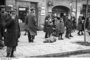 Ein in Lumpen gehülltes Kind liegt auf einem Bürgersteig im Warschauer Ghetto, Mai 1941. Bundesarchiv, Bild 101I-134-0771A-39 / Zermin / CC-BY-SA [CC BY-SA 3.0 de], via Wikimedia Commons