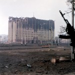 1995: Tschetschenischer Kämpfer steht in der Nähe des zerstörten Regierungsgebäudes in Grosny. By Русский: Фото: Михаил ЕвстафьевEnglish: Photo: Mikhail Evstafiev (Mikhail Evstafiev) [GFDL, CC-BY-SA-3.0 or CC BY-SA 2.5], via Wikimedia Commons