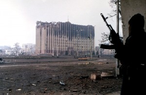 1995: Tschetschenischer Kämpfer steht in der Nähe des zerstörten Regierungsgebäudes in Grosny. By Русский: Фото: Михаил ЕвстафьевEnglish: Photo: Mikhail Evstafiev (Mikhail Evstafiev) [GFDL, CC-BY-SA-3.0 or CC BY-SA 2.5], via Wikimedia Commons