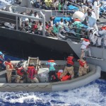 Flüchtlinge klettern nach ihrer Rettung von einem Schlauchboot des US-Marine-Schiffes USS San Antonio (LPD-17) auf ein Patrouillenboot der Republik Malta. By Official U.S. Navy Page from United States of America U.S. Navy photo/U.S. Navy [Public domain], via Wikimedia Commons
